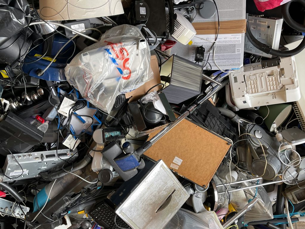 A variety of old home electronics, including a vacuum cleaner, lamps, appliances, computers, screens, keyboards, and a DVD player, ready for recycling to support environmental sustainability.